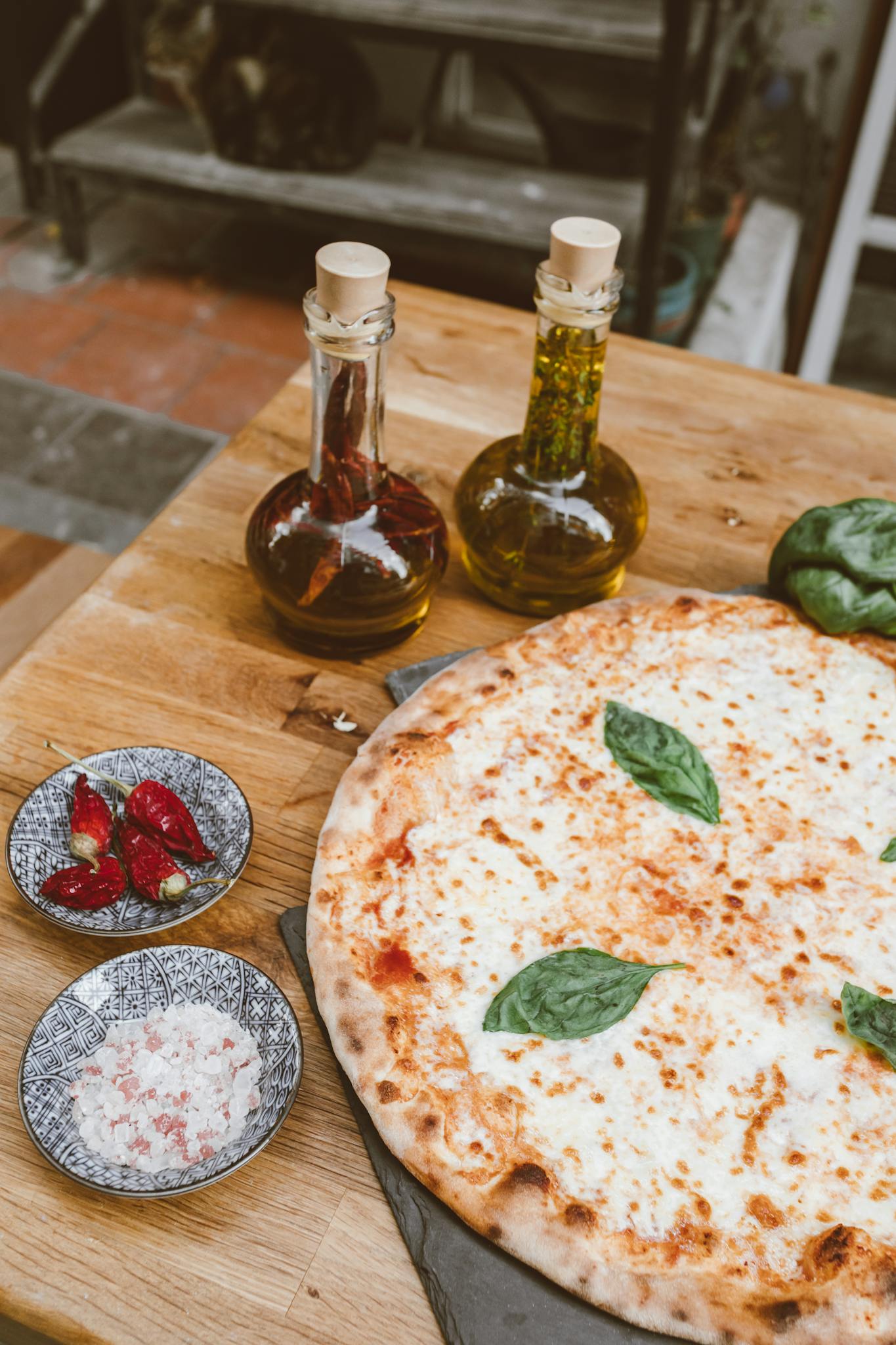 Fresh Margherita pizza with olive oil, spices, and toppings on a wooden table.